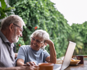 Senior couple smiling as they sit outside in their backyard